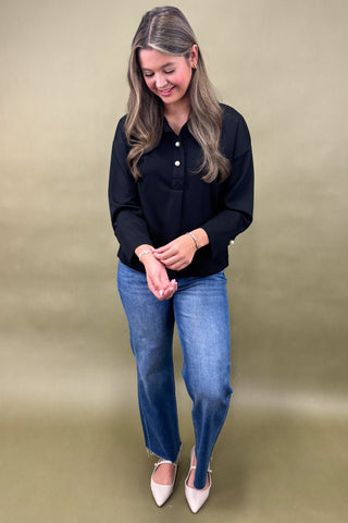 Woman wearing a black shirt and blue jeans against a beige background