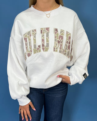 White LULU MAC sweatshirt with camouflage logo lettering, styled with dark wash wide leg jeans.