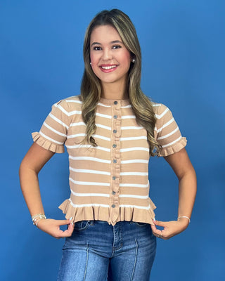 A smiling young woman with blonde-highlighted hair stands against a solid blue studio background wearing a beige and white st
