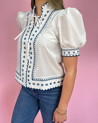 White blouse with blue embroidery and blue jeans on a pink background