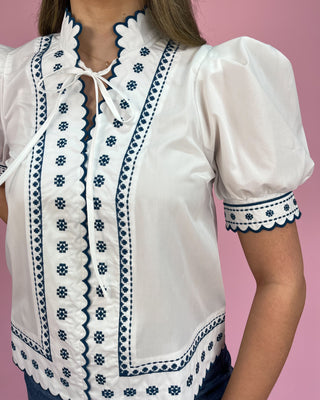 White blouse with blue embroidery on a pink background