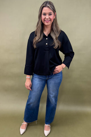 Woman wearing a black blouse and blue jeans against a green background