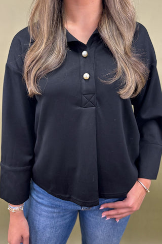 Person wearing a black long-sleeve shirt with white buttons and blue jeans on a beige background