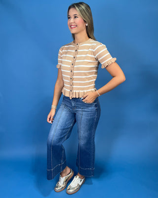 A woman modeling a beige and white striped short-sleeve crop top with ruffle trim and a button-up front, paired with blue j.