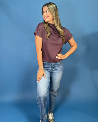 A woman modeling a short-sleeve, high-neck, crewneck t-shirt in a dusty plum purple color