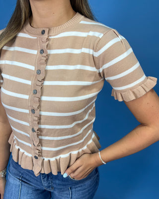 A woman wearing a beige and white horizontally striped short-sleeve knit top with ruffle trim along the front buttons, neck