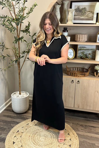 Woman in a black dress standing in a room with a plant and shelves.