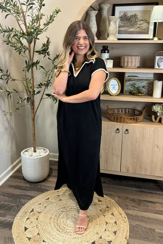 Woman in a black dress standing in a room with a plant and shelves.
