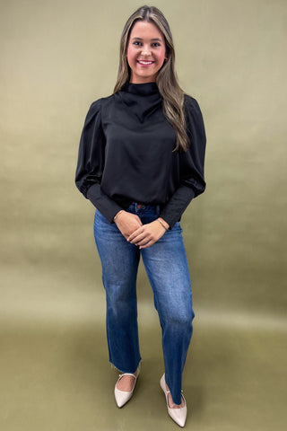 Woman wearing a black blouse and blue jeans against a green background