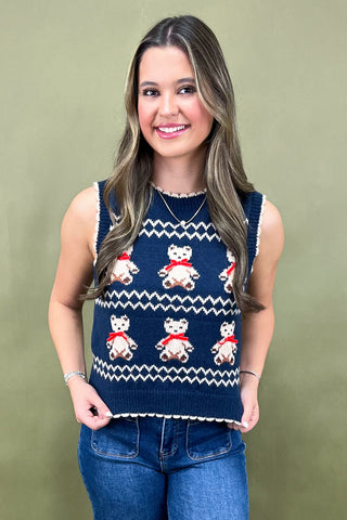 Woman wearing a navy blue sleeveless sweater with teddy bear pattern against a green background