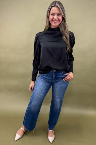 Woman wearing a black top and blue jeans against a beige background