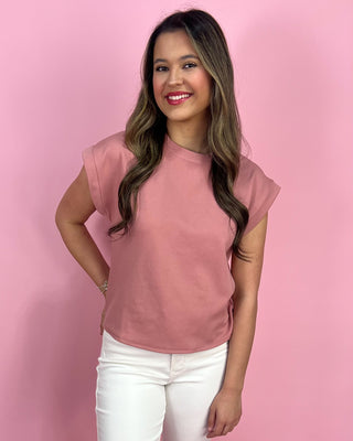 Woman wearing a pink shirt and white pants against a pink background