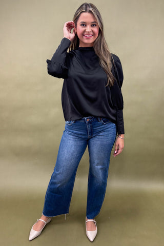 Woman wearing a black top and blue jeans against a green background