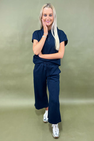 Woman wearing a navy outfit with silver shoes on a green background