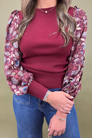 Person wearing a red ribbed sweater with floral sleeves against a beige background
