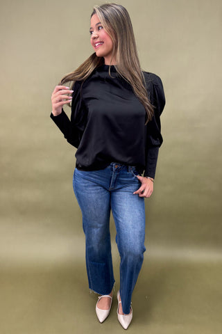 Woman wearing a black blouse and blue jeans against a beige background