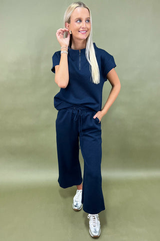 Woman wearing a navy blue outfit with white sneakers on a green background