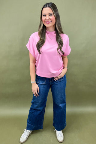 Woman wearing a pink top and blue jeans against a green background