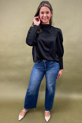 Woman wearing a black top and blue jeans against a green background