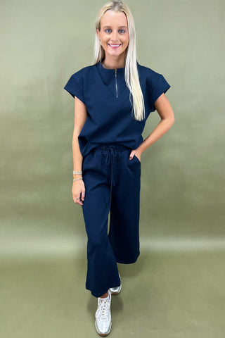 Woman wearing a navy blue outfit with white sneakers on a green background