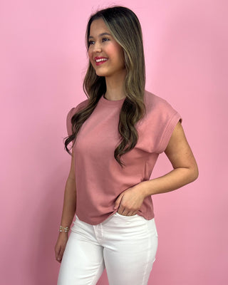 Woman wearing a pink top and white pants against a pink background