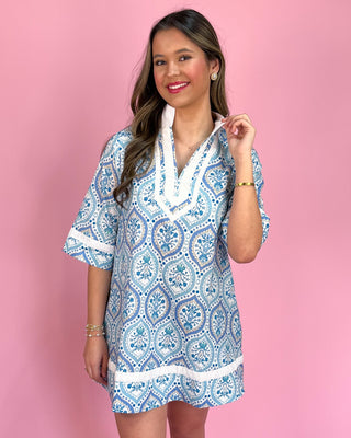 Woman wearing a blue and white patterned dress against a pink background