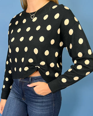 Black long sleeve sweater with cream polka dots, styled with dark wash wide leg jeans and brown flats.