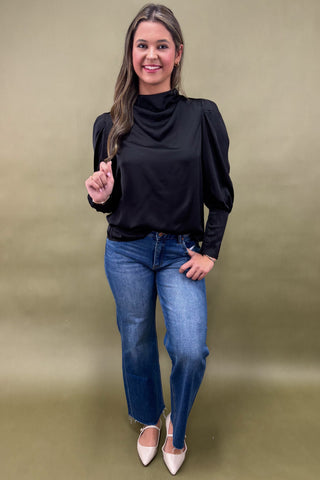 Woman wearing a black top and blue jeans against a beige background