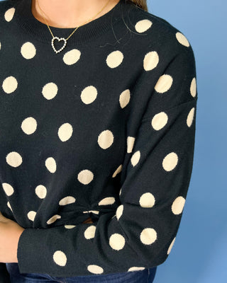 Black long sleeve sweater with cream polka dots, styled with dark wash wide leg jeans and brown flats.