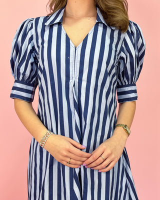 Person wearing a blue and white striped dress against a pink background