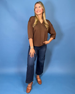 Chocolate brown V-neck three-quarter sleeve top styled with dark wash wide leg jeans and brown flats.