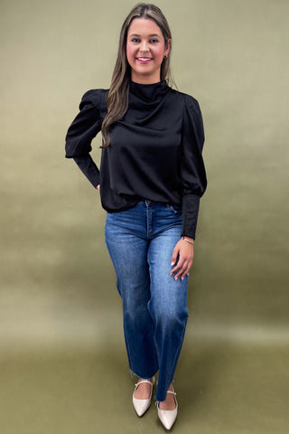 Woman wearing a black top and blue jeans against a green background