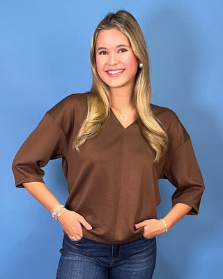 Chocolate brown V-neck three-quarter sleeve top styled with dark wash wide leg jeans and brown flats.