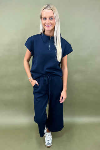 Woman wearing a navy outfit with white sneakers against a green background