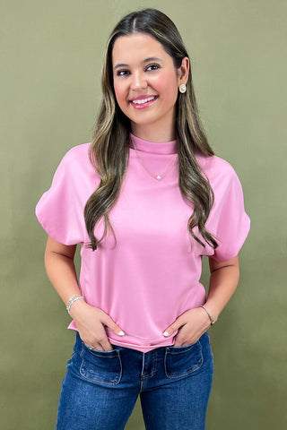 Woman wearing a pink top and blue jeans against a green background