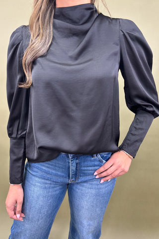 Person wearing a dark gray long-sleeve top and blue jeans against a beige background