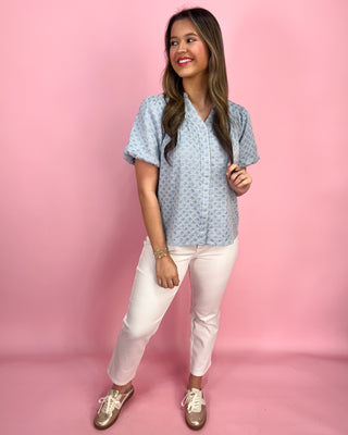 Woman wearing a blue patterned shirt and white pants against a pink background