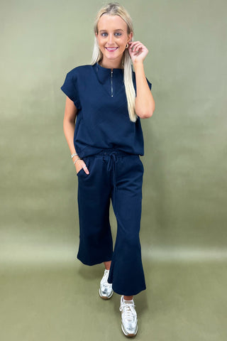 Woman wearing a navy outfit with wide-leg pants against a green background
