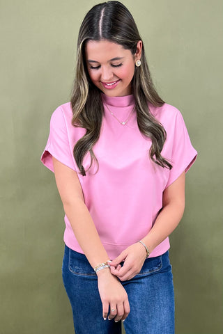 Woman wearing a pink blouse and blue jeans against a green background