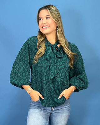 A woman wearing a dark green patterned blouse with a tie-neck detail and voluminous sleeves