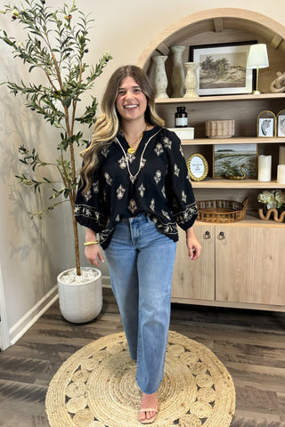 Woman standing in a room with wooden flooring and a plant, smiling.