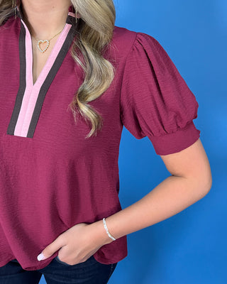 Burgundy puff sleeve blouse with a V-neckline and contrasting pink and brown trim for a polished feminine look.