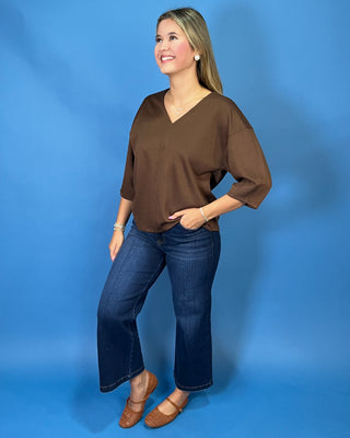 Chocolate brown V-neck three-quarter sleeve top styled with dark wash wide leg jeans and brown flats.