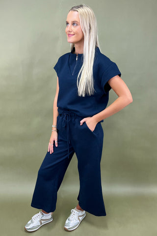 Woman wearing a navy blue outfit with white sneakers on a green background