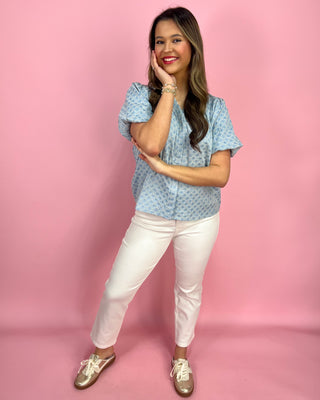 Woman wearing a blue patterned blouse and white pants against a pink background