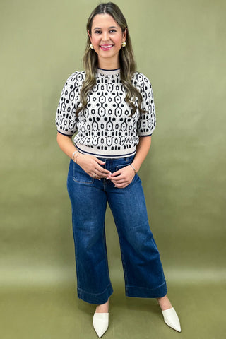 Woman wearing a patterned top and blue jeans against a green background