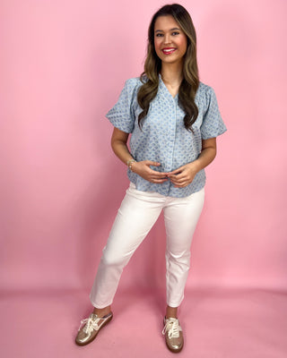 Woman wearing a blue patterned blouse and white pants against a pink background