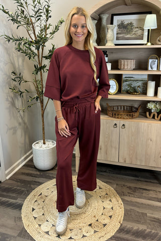 Woman in burgundy outfit standing in a room with wooden shelves and decor.