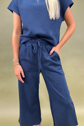 Person wearing a blue textured outfit with wide-leg pants on a beige background