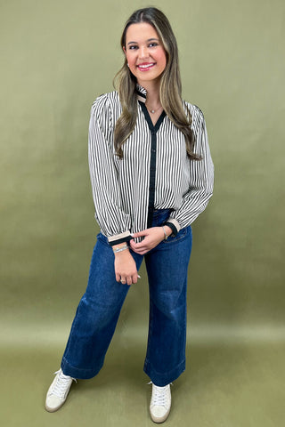 Woman wearing a striped shirt and blue jeans against a green background
